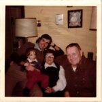 Boy holding a baby in a living room with his grandparents in 1970s